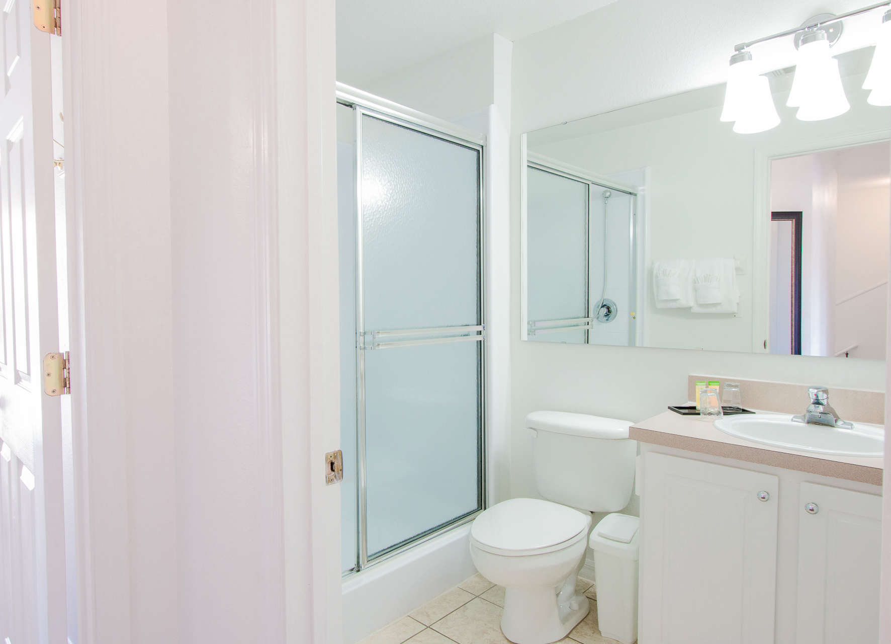 A clean and simple bathroom with white walls, a glass shower door, a toilet, and a sink with a mirror above it.