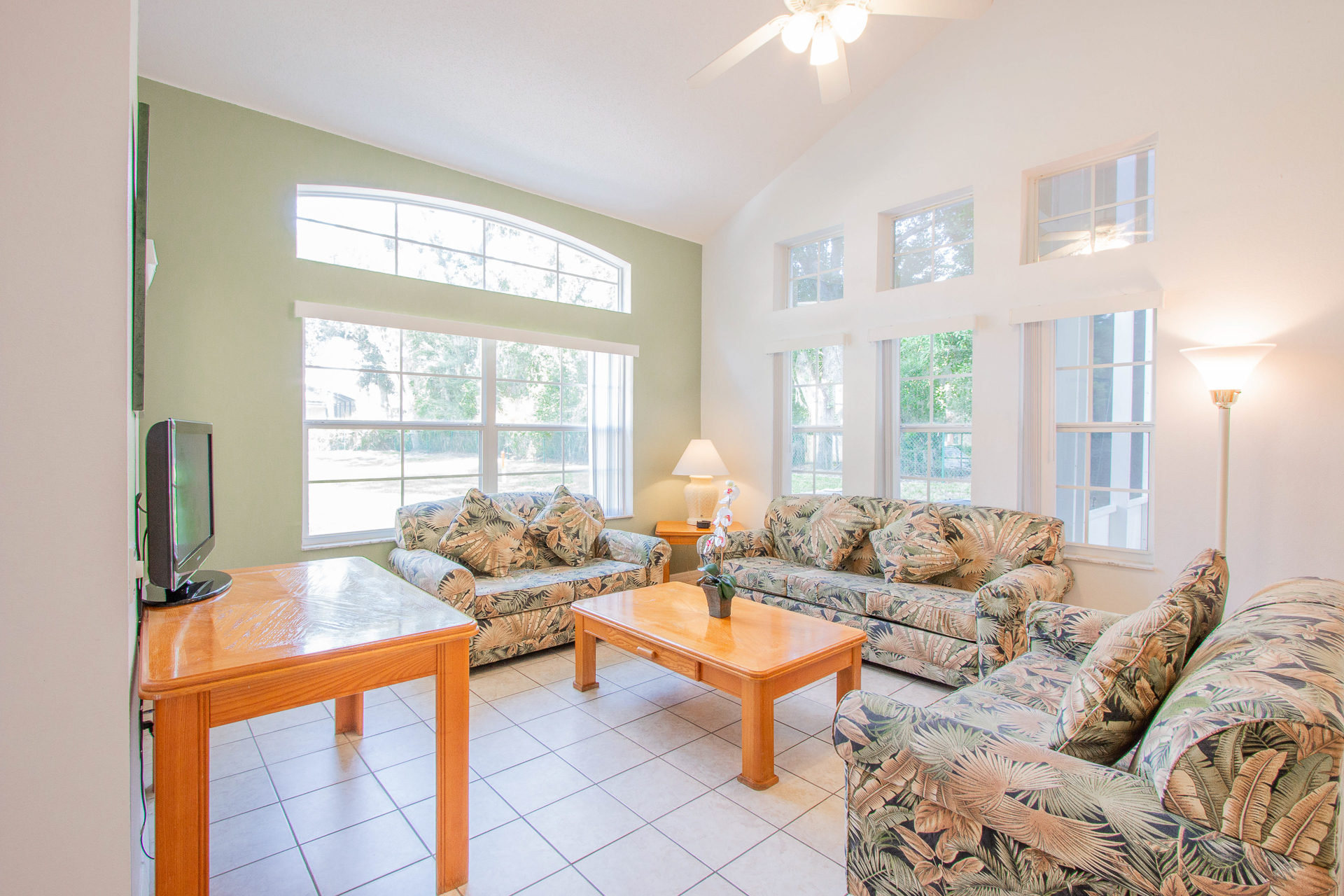 A bright and airy living room with two floral couches, a wooden coffee table, and a TV on a wooden stand.