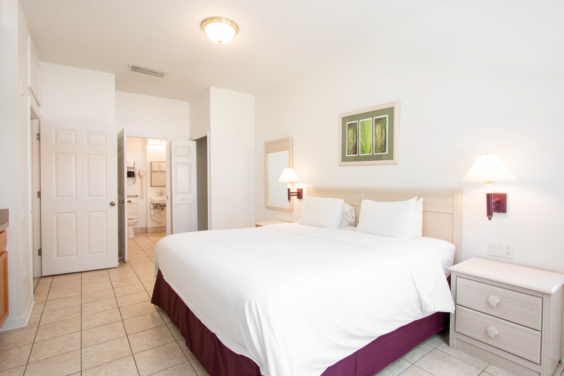 A wide-angle view of a hotel room with a large bed, nightstand, and lamp.